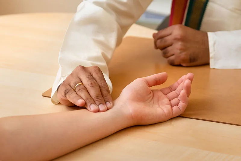 Three fingers resting on a wrist, a pulse reading